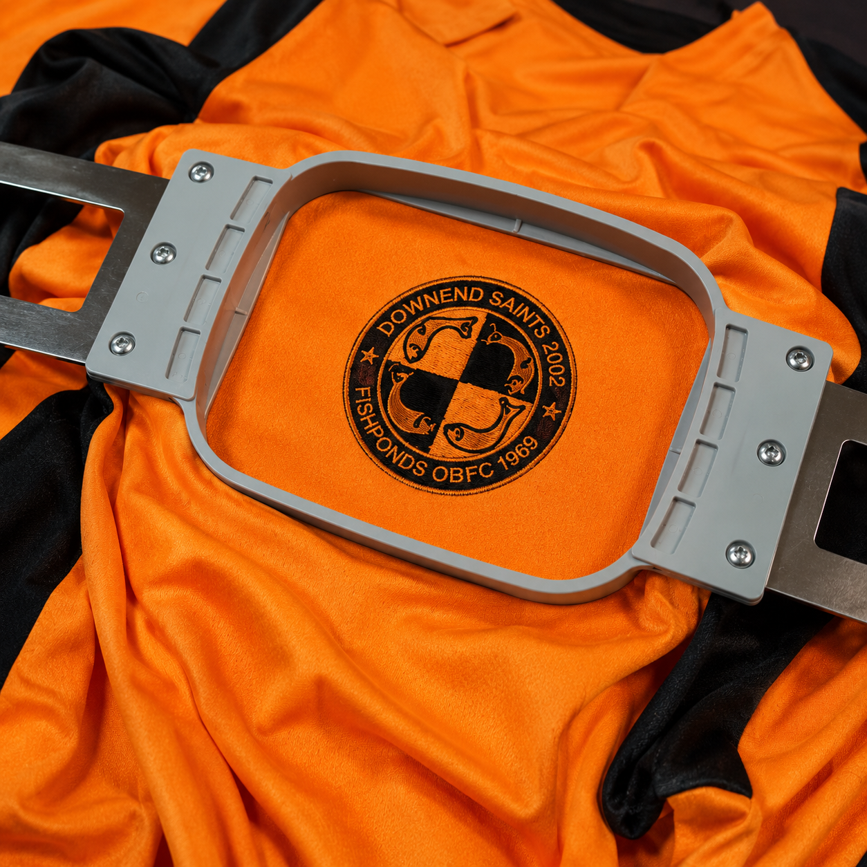 Downend Saints & Fishponds OB FC badge being embroidered onto an orange shirt